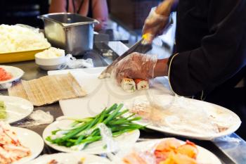 Preparing of traditional Japanese sushi with salmon, cook cuts roll of rice and fish. Selective focus