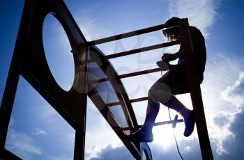 Silhouette of a little girl  on a outdoor playground equipment above blue sky background