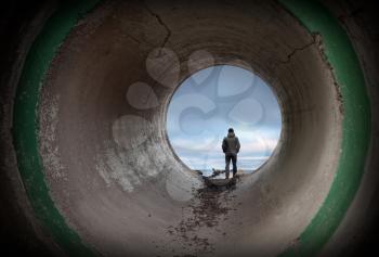 Man looks at horizon in the end of dark concrete tunnel
