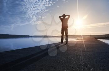 A man stands on the concrete pier starring at the Sun