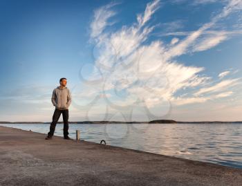 A man stands on the concrete pier starring at the sea under beautiful windy clouds