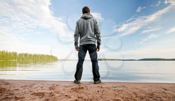 A man stands on the sand lake coast starring at the horizon