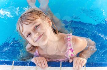 Portrait of a slightly smiling little blond beautiful Russian girl in a pool