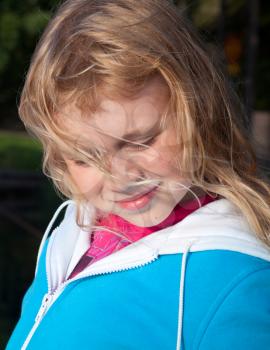 Little beauty girl smiles with closed eyes and blond hairs on wind