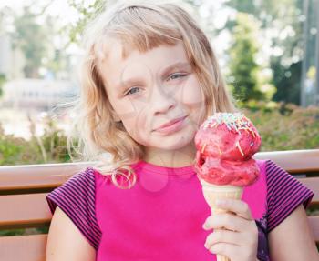 Little girl with big fruit ice-cream seats on wooden bench in park