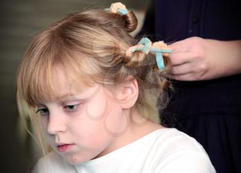Little blond Russian girl with curlers on hair and hands of hairdresser