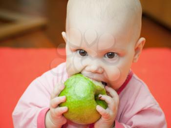 Little baby in a pink jacket eats green apple