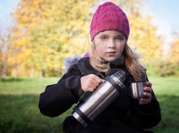 little beautiful blond girl pours tea from a thermos in autumnal park