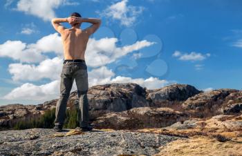 Topless strong man relaxed stands on the mountain and looks over horizon