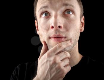Young thinking Caucasian man isolated on black background