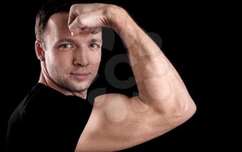 Young sporty man shows biceps, portrait isolated on black background