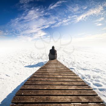 Man in black sit on old wooden pier. Winter coast of frozen Baltic Sea
