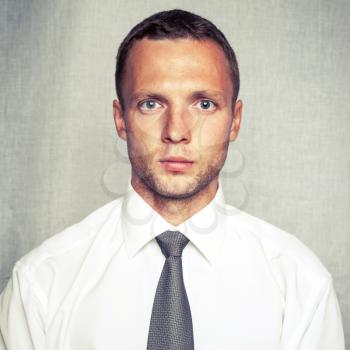 Young serious man in white shirt with tie over gray background. Closeup square studio portrait with vintage tonal correction old style photo filter