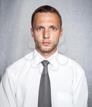Young serious man in white shirt with tie over gray background. Studio portrait