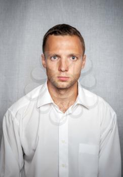 Young serious man in white shirt over gray background. Studio portrait