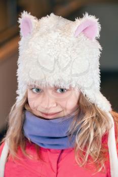 Little blond girl in fun white artificial fur hat. Closeup outdoor portrait