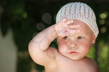 Little tired baby girl in white hat wipes off the sweat from his forehead