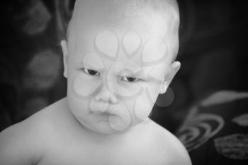 Funny angry baby girl close-up monochrome portrait on dark blurred background