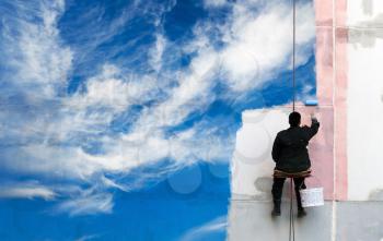 Painter paints bright blue sky on the urban wall
