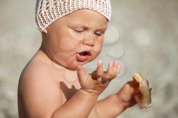 Little Caucasian baby eats croissant on the beach