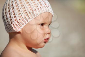 Outdoor profile portrait of curious Caucasian baby girl in white hat on the beach