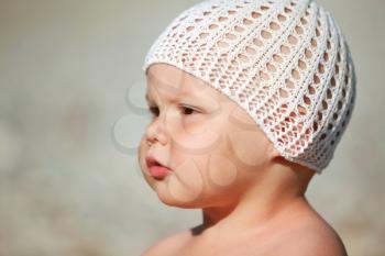 Outdoor closeup portrait of serious Caucasian baby girl in white hat on the beach