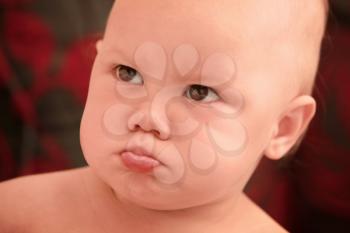 Funny angry Caucasian baby girl close-up portrait on dark blurred background