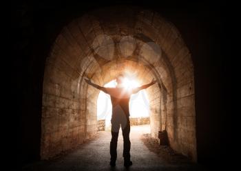 Man stands inside of old dark tunnel with shining sun in the end