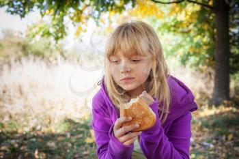 Little blond girl on a picnic in autumn park eats small pies