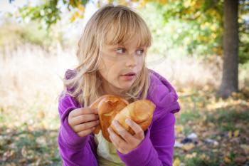 Little blond girl in autumn park holds small pies in hands