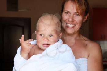 Young Caucasian mother holds with smile her funny baby in white cotton towel after the bath