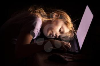 Little blond girl sleeping on a laptop in dark room at night