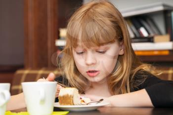 Little blond girl eats cake with tea