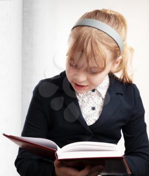Closeup portrait of blond Caucasian schoolgirl reading textbook