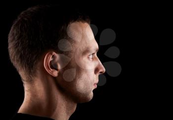 Profile portrait of serious young Caucasian man isolated on black background
