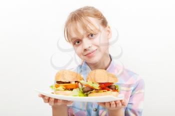 Little smiling blond girl with homemade hamburgers on white plate