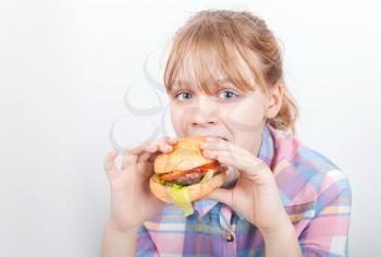 Little blond girl eats hamburger above white wall