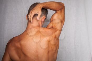 Back of young muscular man above gray background