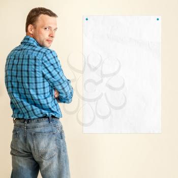 Young Caucasian man in blue shirt with empty white paper on the wall