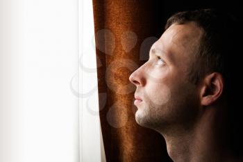 Young Caucasian man looking in bright window, closeup profile portrait 