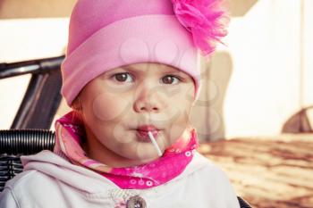 Closeup portrait of baby girl in pink eating lollipop