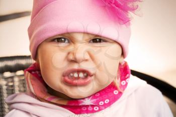 Closeup portrait of funny angry baby girl in pink