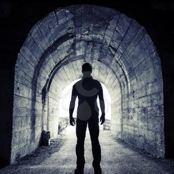 Young man stands in dark tunnel and looks in the glowing end