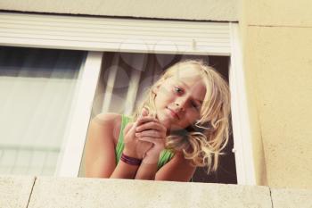 Little blond Caucasian girl in window, outdoor vintage toned portrait