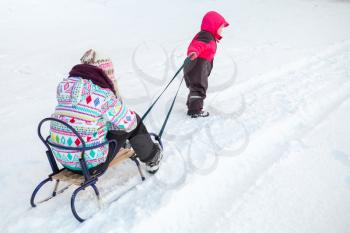 Little baby girl in pink pulling a sled with her big sister on snowy road