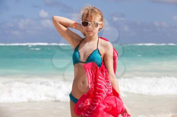 Outdoor portrait of beautiful Caucasian teen girl in blue swimsuit and red shawl standing on the ocean coast