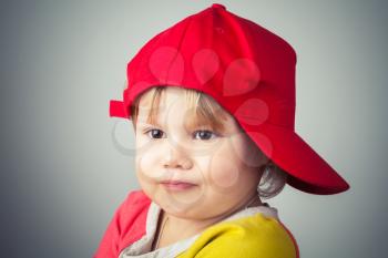Studio portrait of funny baby girl in red baseball cap over gray wall background. Vintage style, photo filter effect