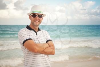 Outdoor portrait of young smiling Caucasian man in white hat and sunglasses standing on the sea coast