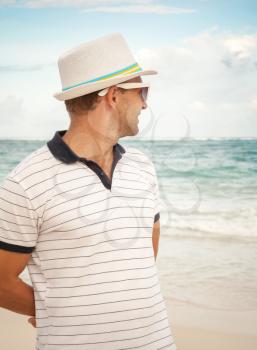 Young smiling Caucasian man in white hat and sunglasses looks forward on the summer ocean coast
