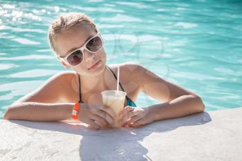 Little blond girl with glass of cocktail in a swimming pool